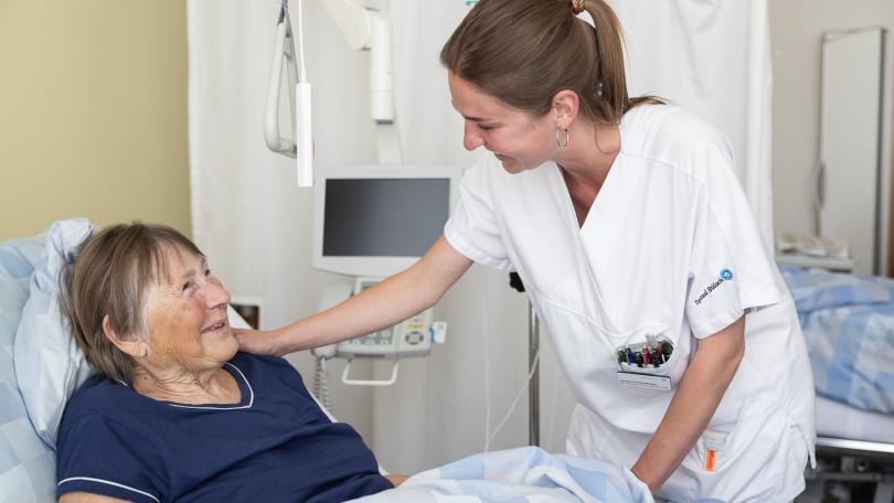 Ältere Patientin im Spitalbett wird von Pflegerin betreut