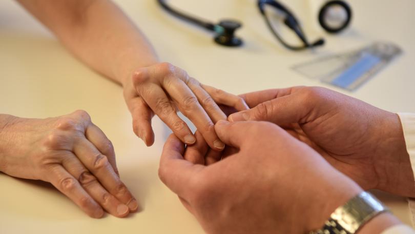 Ärztliche Fachperson hält rheumatische Hand einer Patientin.