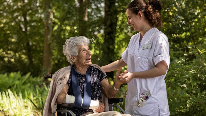 Pflegerin hält die Hand einer Patientin im Rollstuhl.