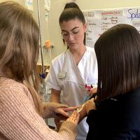 Zwei Schülerinnen informieren sich bei einer Fachfrau Gesundheit in Ausbildung über den Pflegeberuf